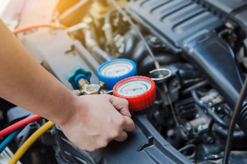 A technician connecting A/C manifold gauges under the hood