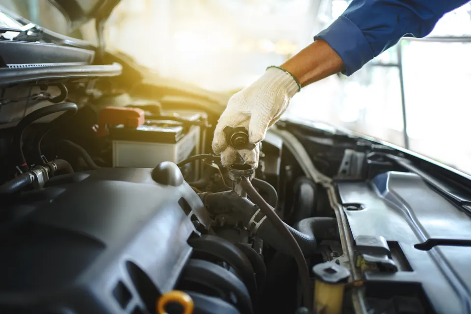 A technician checking the coolant reservoir under the hood