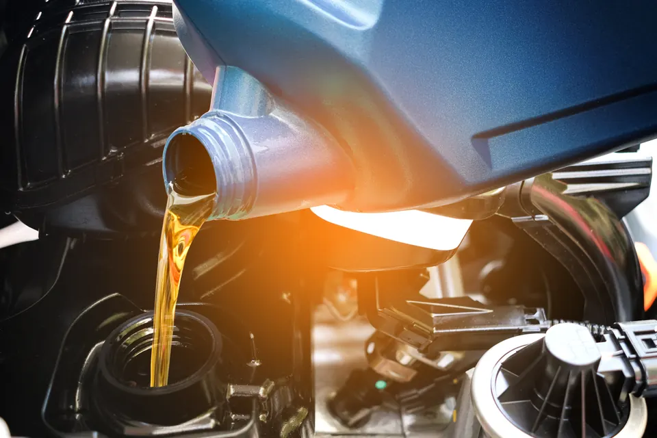 Motor oil pouring from a blue bottle into an engine