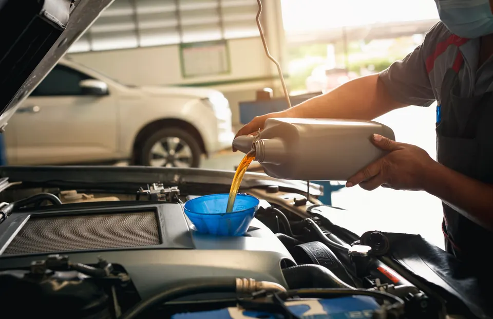 A technician pouring oil through a funnel into an engine in a service bay