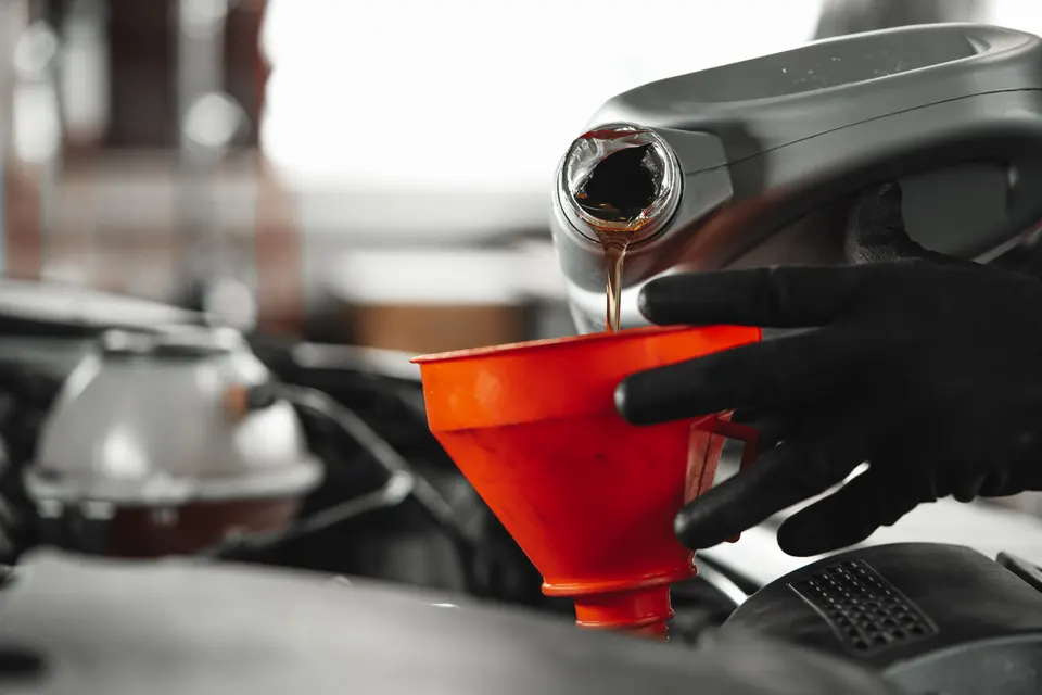 Gloved hands pouring new oil through an orange funnel into an engine