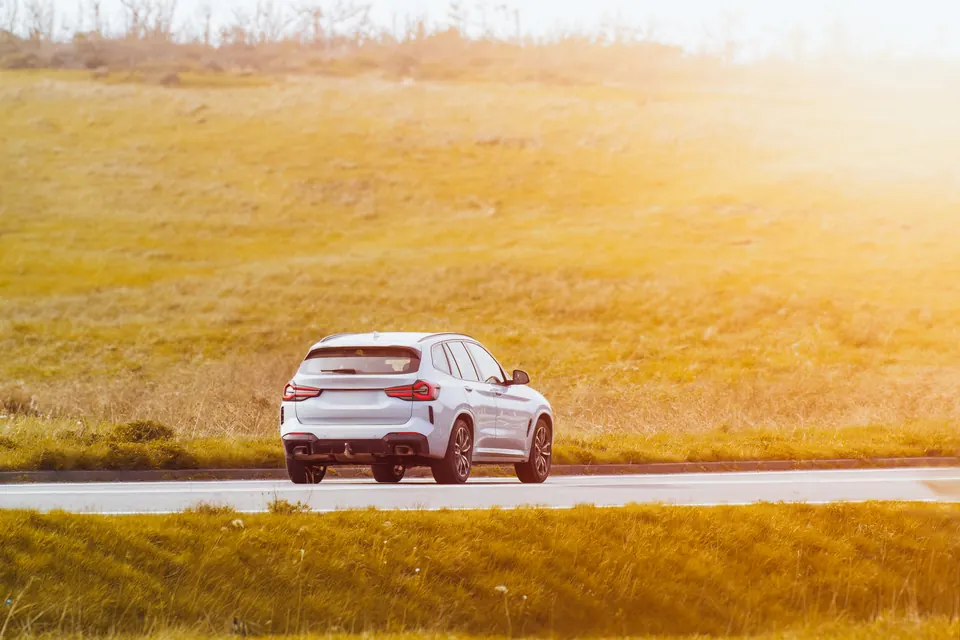 A white SUV driving a two-lane road past golden grassland