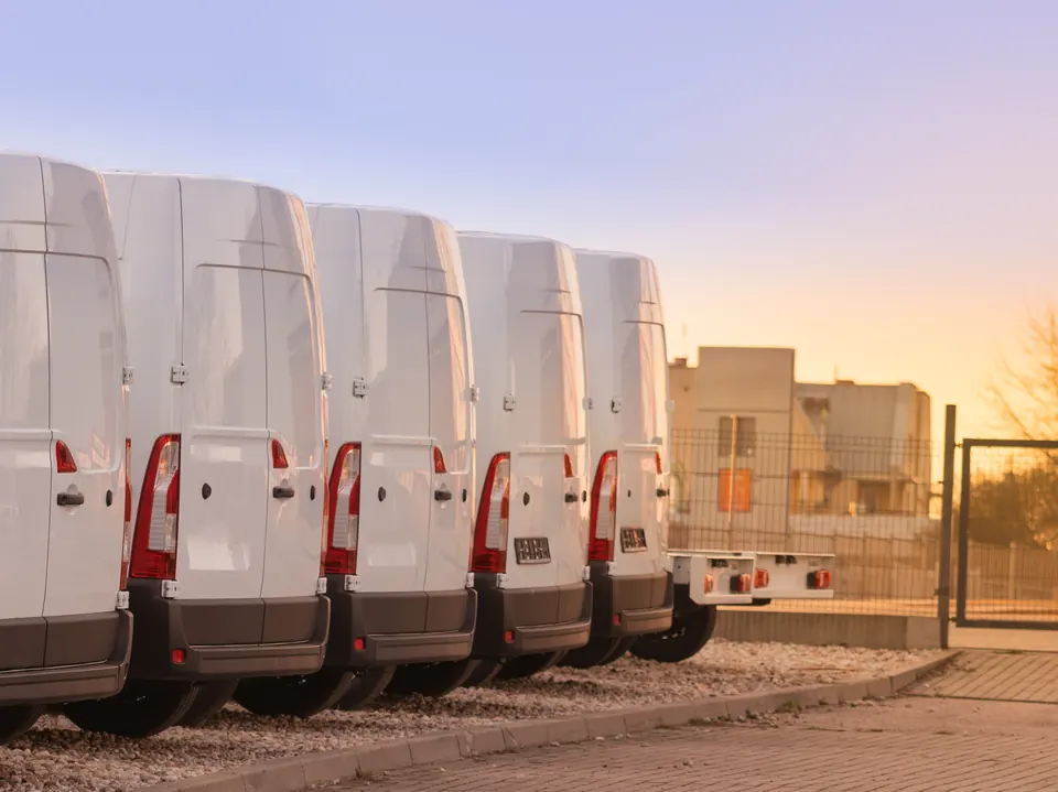 A row of white delivery vans parked at sunset