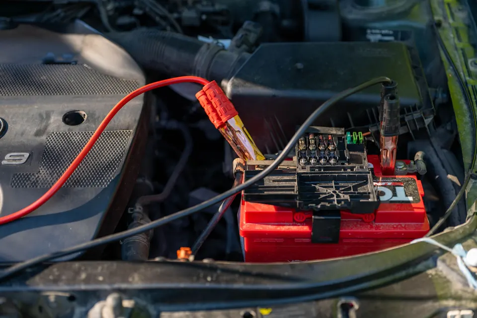A battery charger clamped to a car battery under the hood