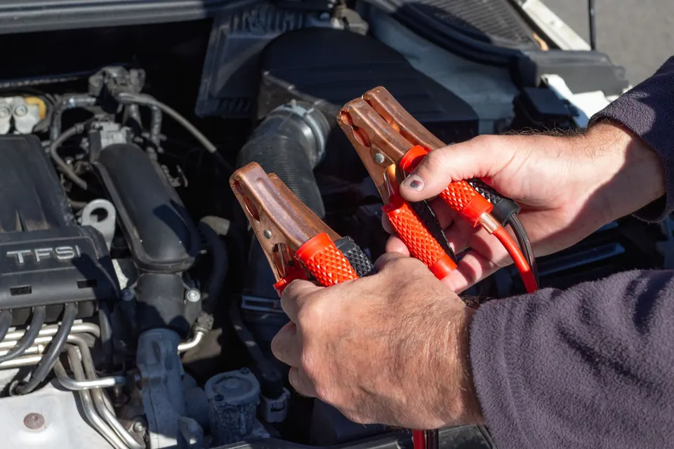 Hands holding jumper cable clamps beside an engine