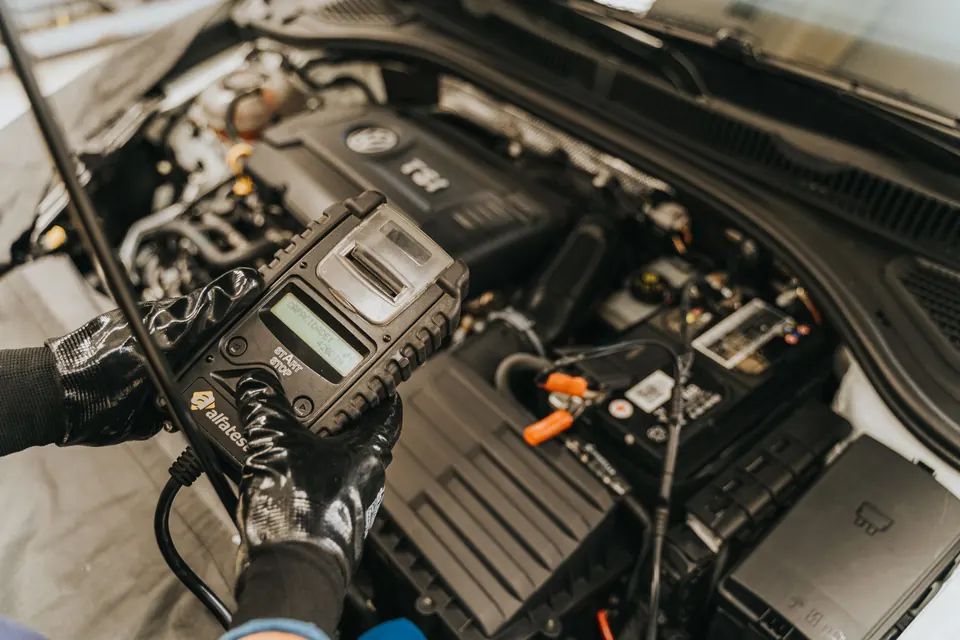 A handheld battery and charging tester connected under the hood