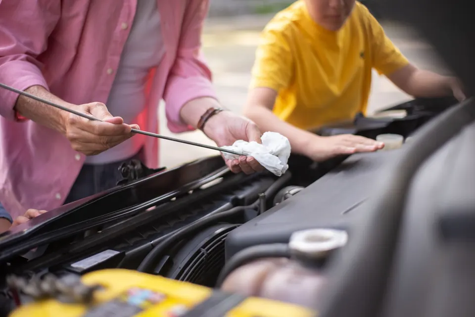 A parent and a teenager checking the oil dipstick together