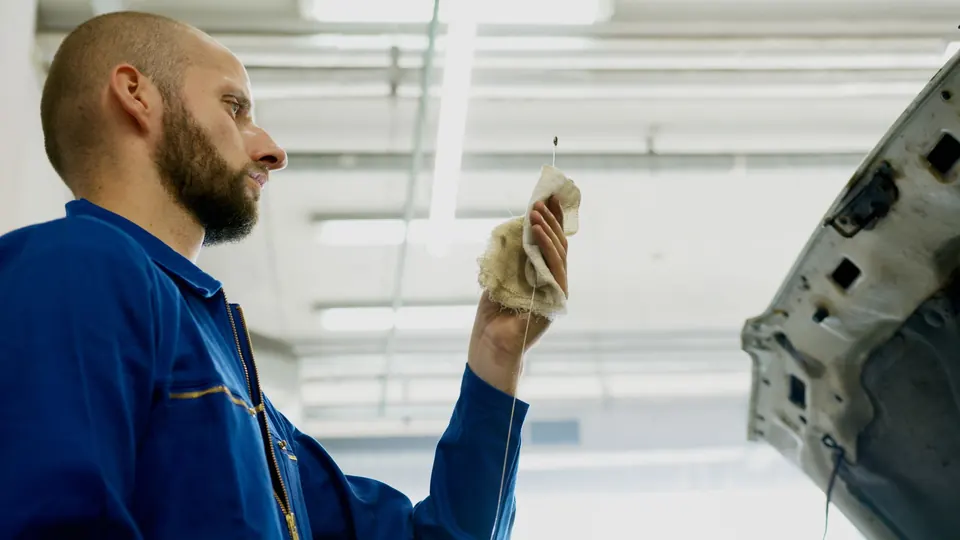 A technician in blue coveralls reading the oil on a dipstick