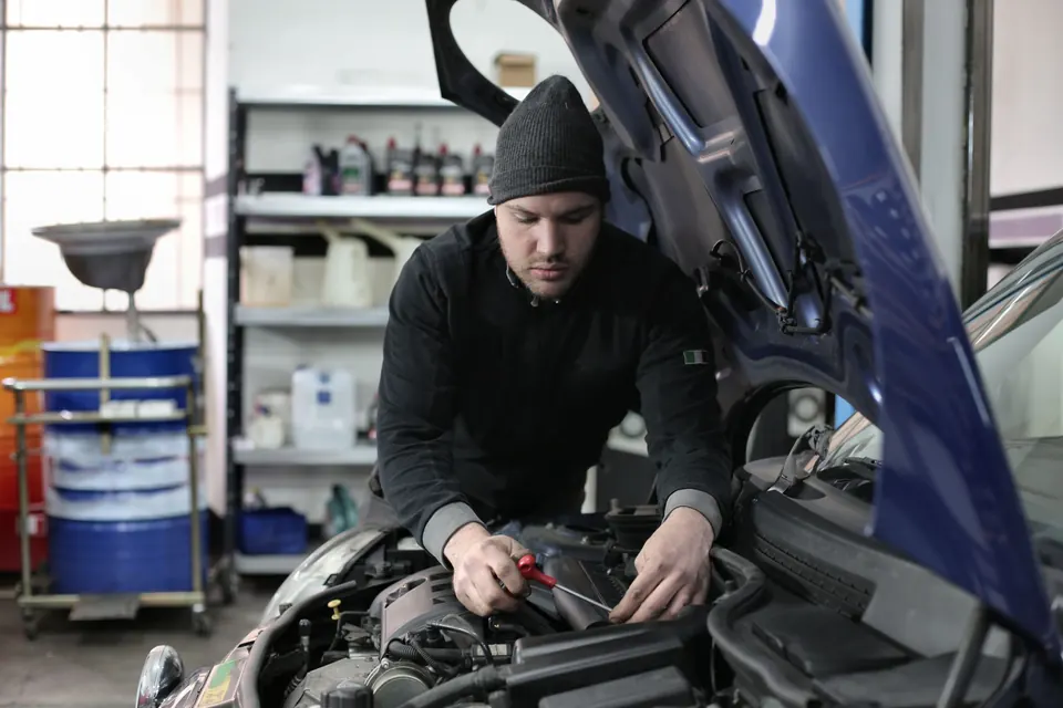A mechanic in a knit cap working in the engine bay of a blue car