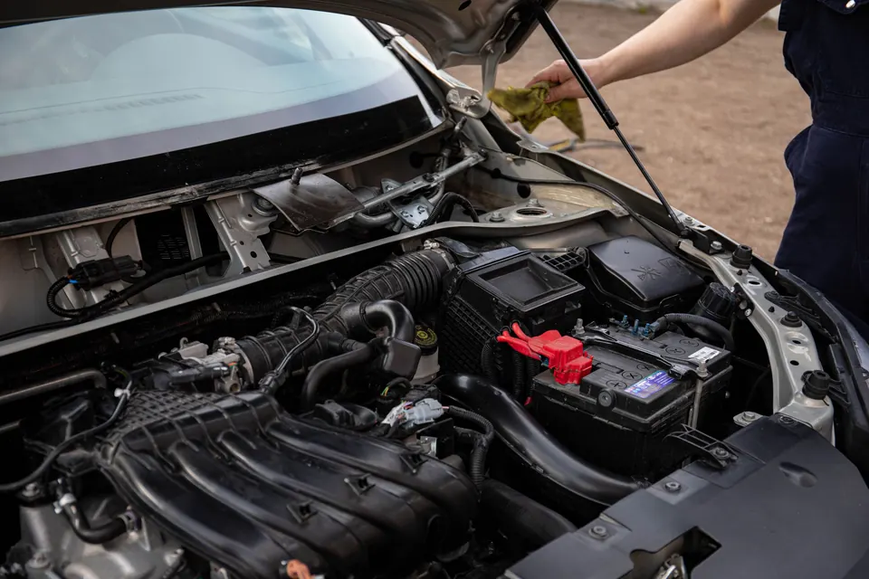 A technician checking the engine bay and battery of a compact car