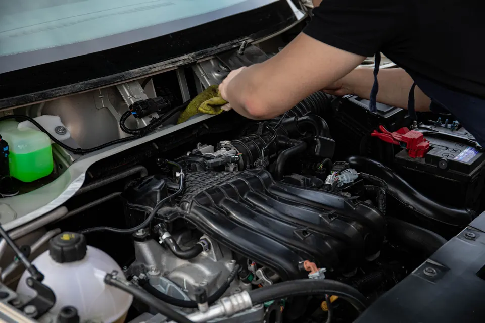 A technician reaching into an engine bay beside the coolant reservoir