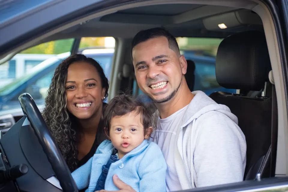 A family smiling from the front seat of their car