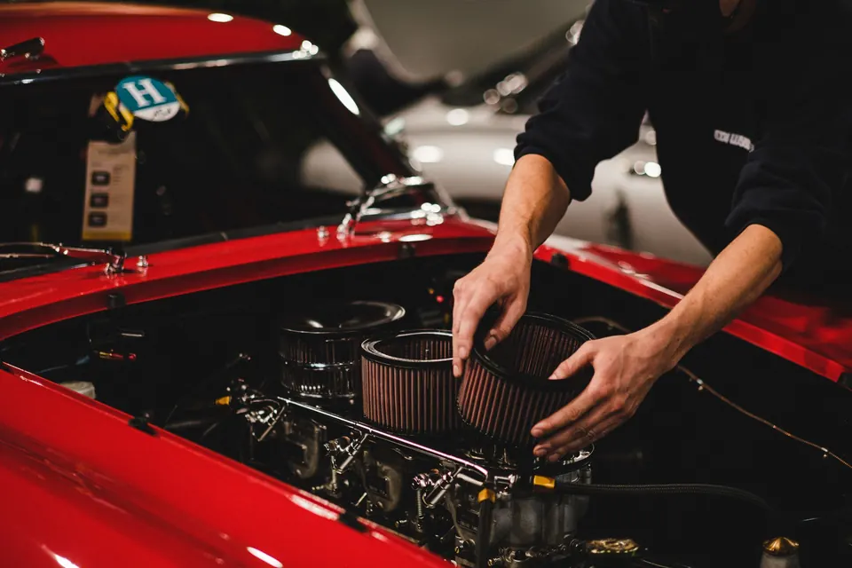 A technician fitting an air filter on a red car's engine