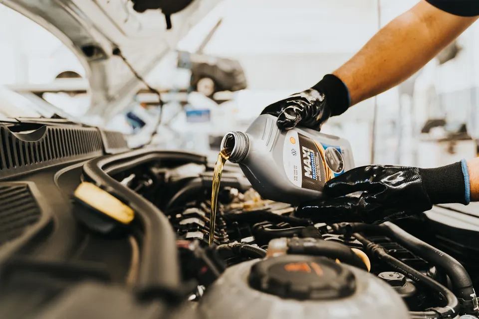 A technician pouring oil into an engine under an open hood