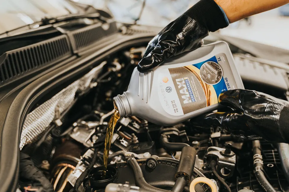 Gloved hands pouring fresh motor oil into an engine