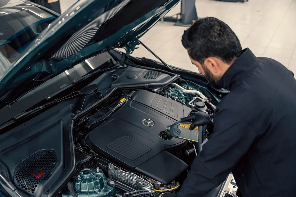 A technician topping up engine oil under the hood of a dark SUV