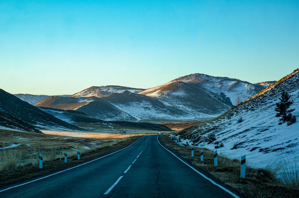 A two-lane highway through snow-dusted hills