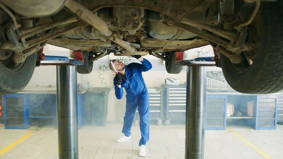 A technician inspecting the underside of a car on a lift