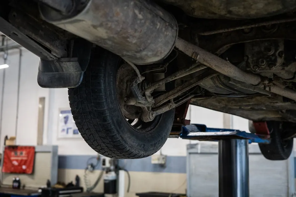 A car's suspension and tire seen from below on a lift
