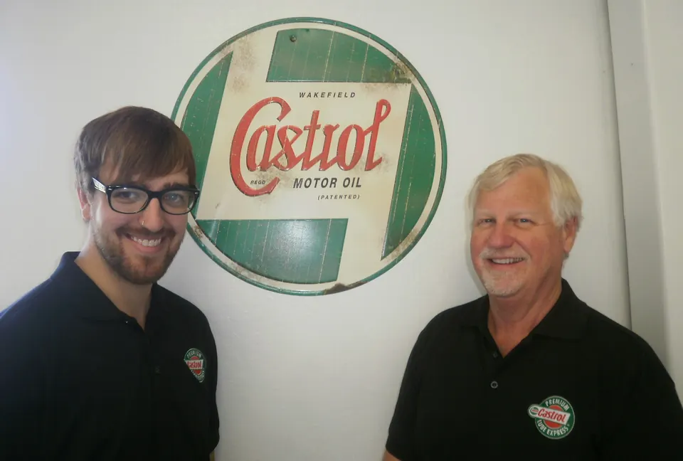 Two Xpress team members smiling in front of a vintage motor oil sign at the Carson City service center